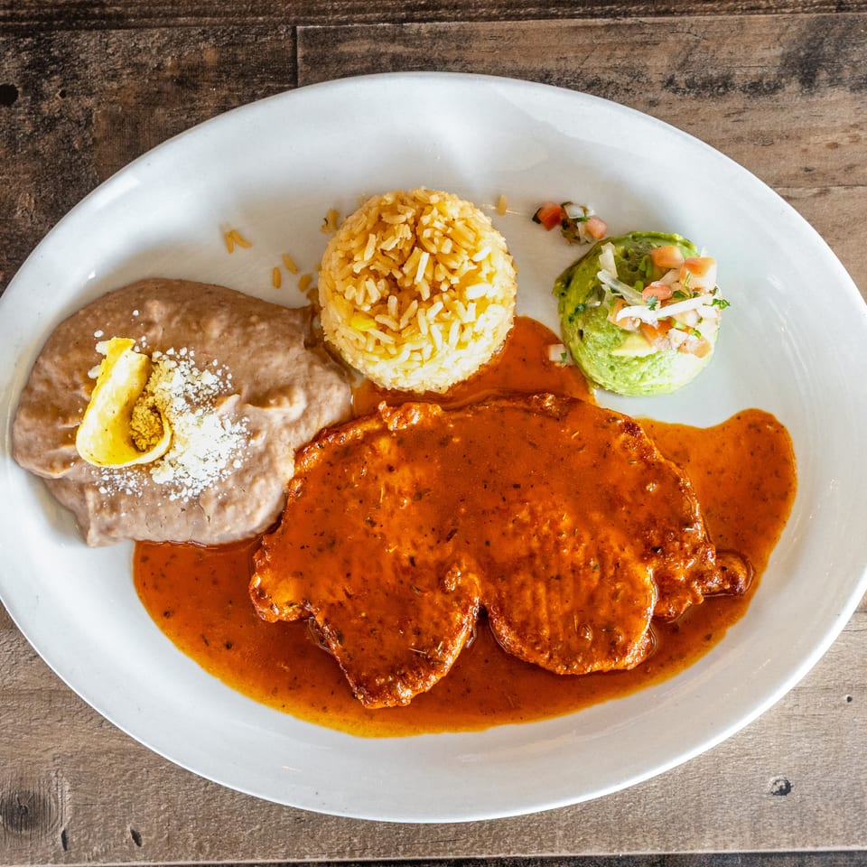 Mexican plate with enchiladas in red sauce, refried beans, yellow rice, guacamole, pico de gallo, and lime.