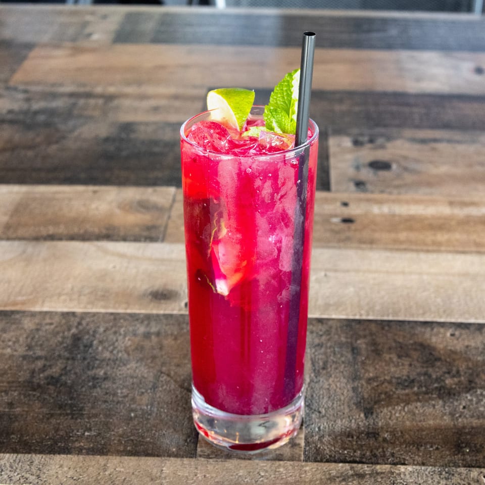 Vibrant red iced cocktail garnished with lime and mint, served with a metal straw on a rustic wooden table.