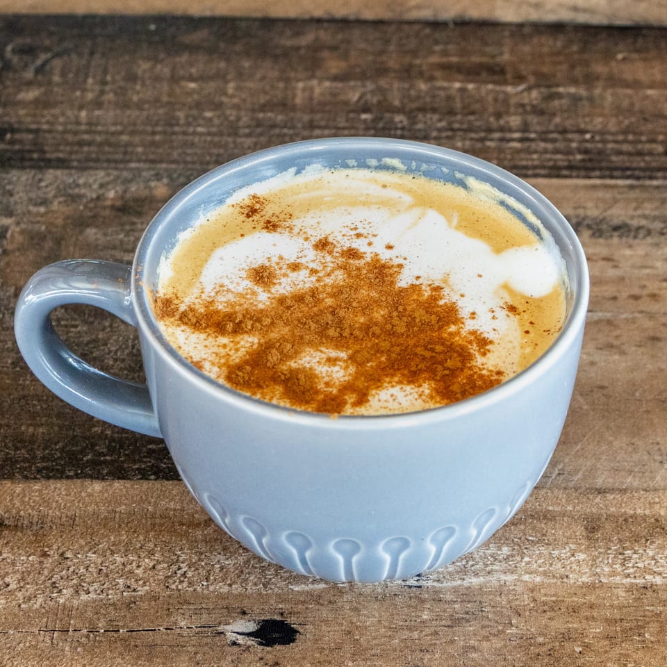 Blue ceramic cup of frothy coffee dusted with cinnamon on a rustic wooden table.