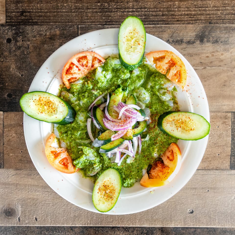 Overhead view of a green-sauced salad topped with cucumber, red onion, and tomato wedges on a white plate.