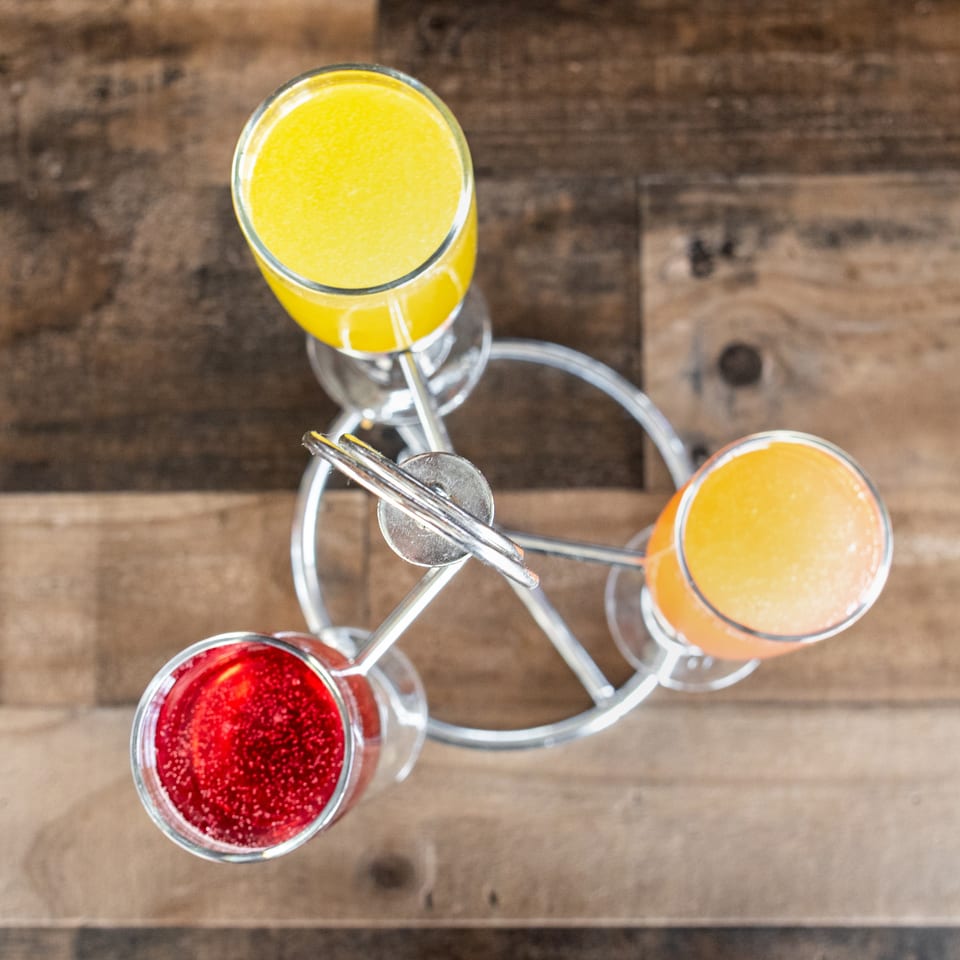 Three colorful cocktails—yellow, orange, and red—arranged in glasses on a rustic wooden table.