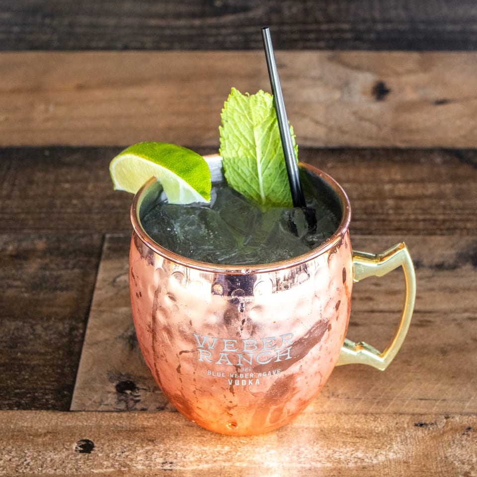 Copper mug filled with an iced mint cocktail, garnished with lime and mint on a rustic wooden table.