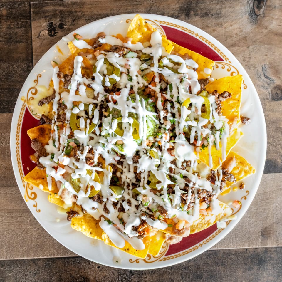 Loaded nachos topped with seasoned meat, vegetables, jalapeños, and drizzled white sauce on a decorative plate.
